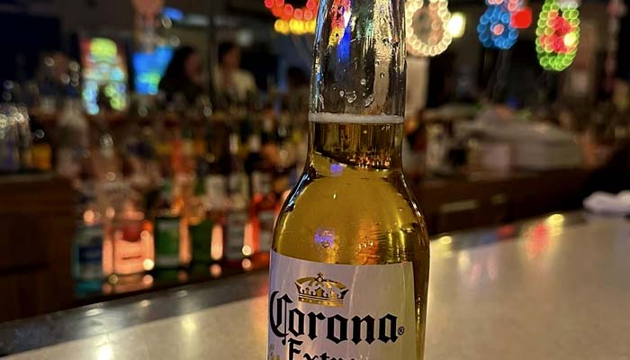 A bottle of Corona Extra beer sits on the Sherwood Bar counter at The Granary Supper Club, with colorful, blurry lights and bottles in the background, creating a lively, festive atmosphere—perfect for enjoying the best food.