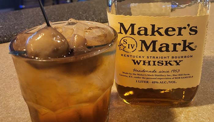 A glass filled with ice and a brown liquid sits next to a bottle of Maker’s Mark Kentucky Straight Bourbon Whisky on the Sherwood Bar countertop at Sherwood Restaurant.