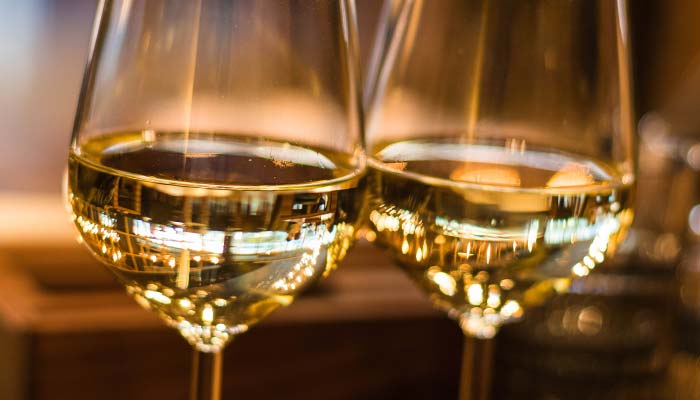 Two glasses of white wine are close together, with reflections of light and a warm, blurred background suggesting an intimate setting—perfect for a celebration at Sherwood Restaurant or The Granary Supper Club serving the best food.