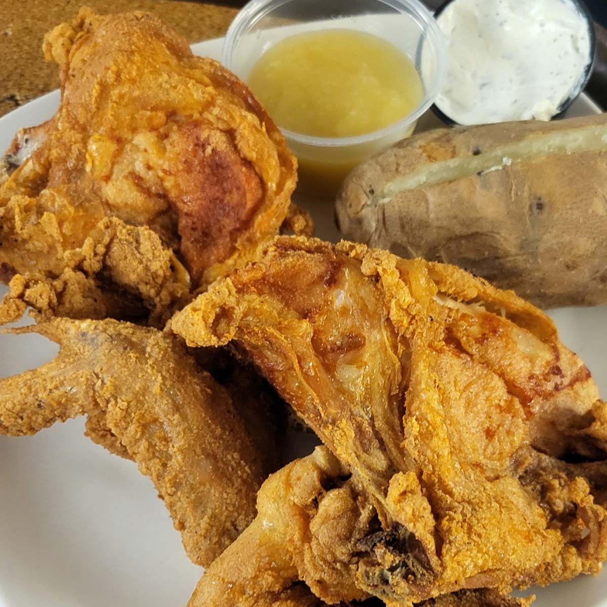 Enjoy the best food at Sherwood Bar—a plate featuring crispy fried chicken, a baked potato with sour cream, and a small container of applesauce.
