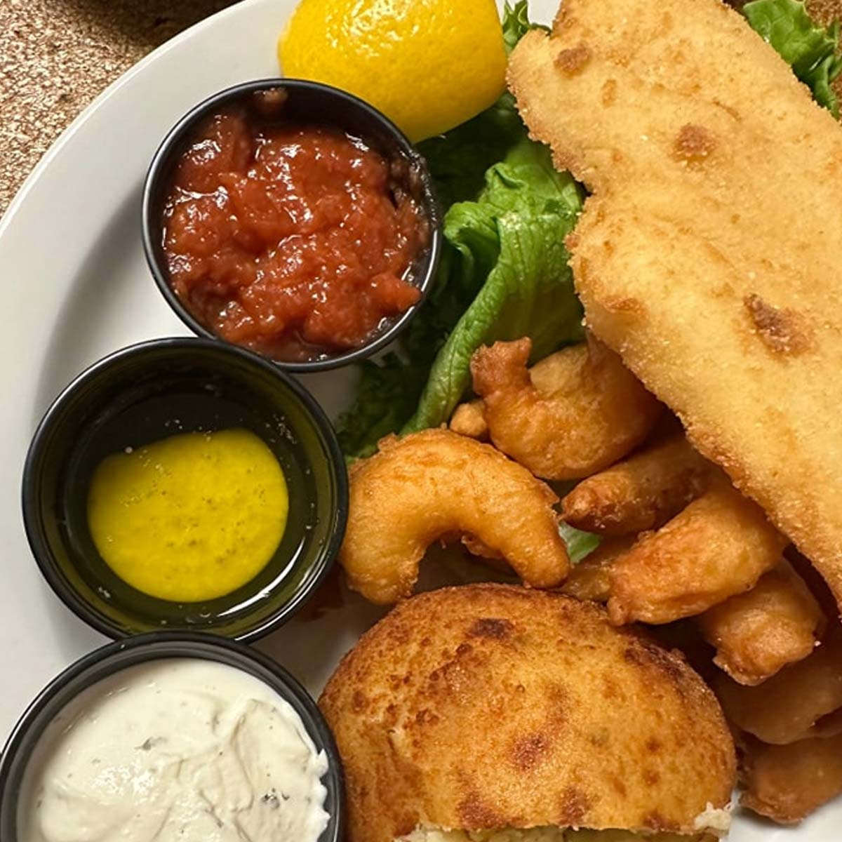 Enjoy a plate at Sherwood Restaurant featuring breaded fried fish, shrimp, a biscuit, lettuce, lemon wedge, and three dipping sauces: cocktail sauce, melted butter, and tartar sauce—some of the best food in town!.