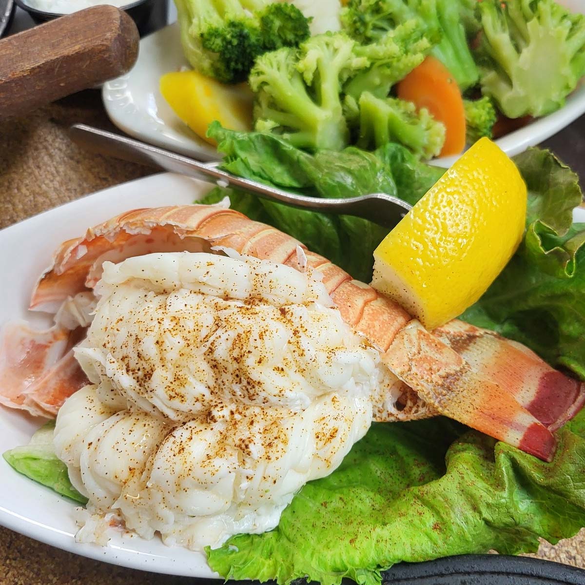 Steamed lobster tail with seasoning on a bed of lettuce, garnished with a lemon wedge and served alongside steamed broccoli, carrots, and yellow squash—a true taste of the Best Food at The Granary Supper Club.