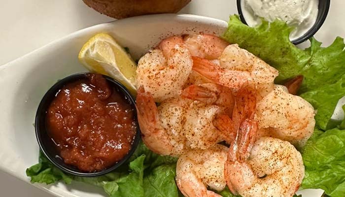 A plate of seasoned shrimp served on a bed of lettuce with a lemon wedge, cocktail sauce, and tartar sauce—just one example of the Best Food you’ll find at Sherwood Restaurant.
