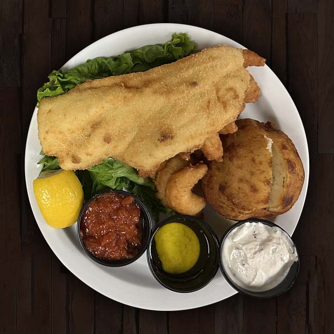 A plate from The Granary Supper Club features a large breaded fish fillet, hushpuppy, lemon wedge, leafy greens, cocktail sauce, mustard, and tartar sauce in small cups—all served on a dark wooden surface. Enjoy the best food in town!.