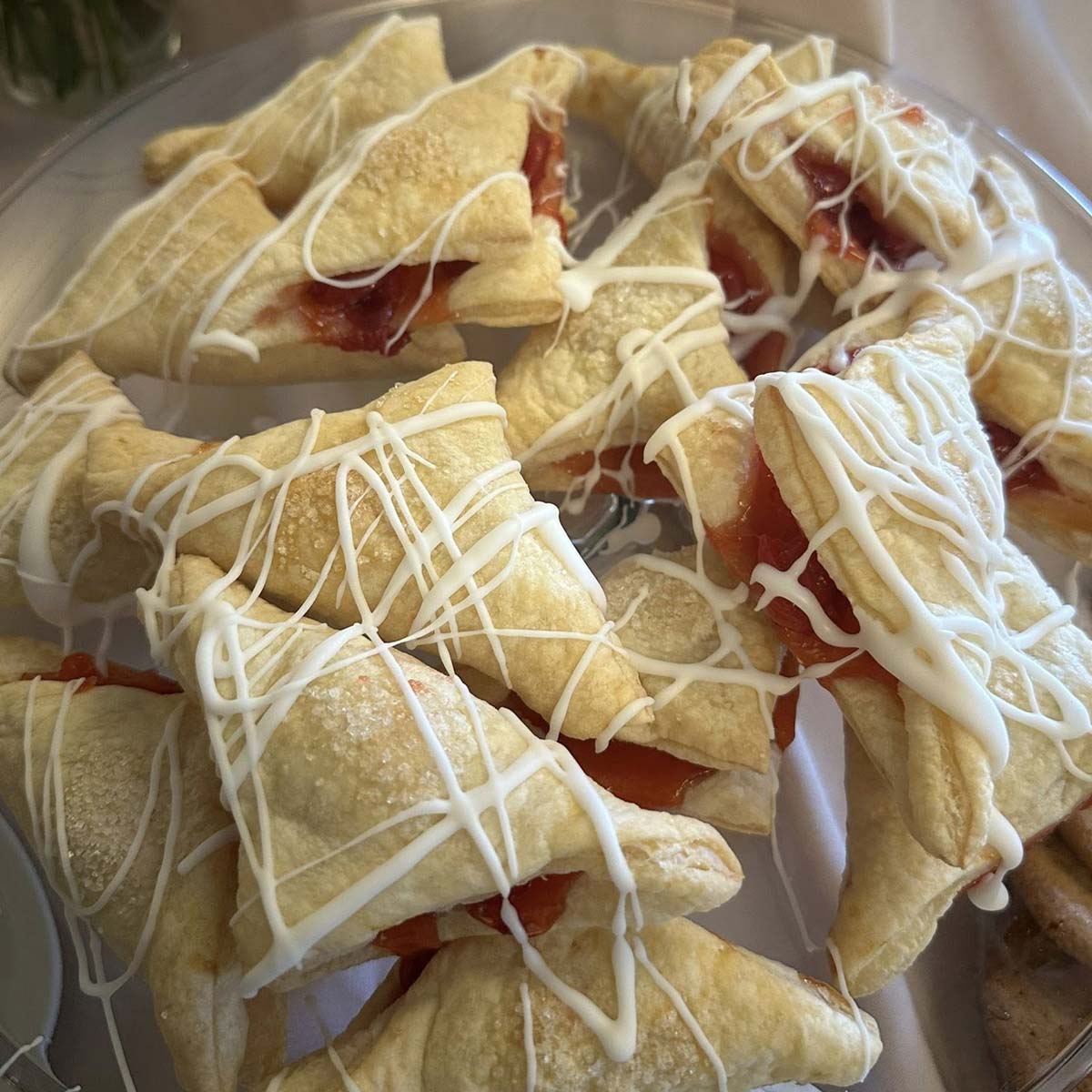 A plate of triangular puff pastries filled with red fruit jam and drizzled with white icing, arranged closely together on a clear dish, just like the delightful treats served at Sherwood Bar.
