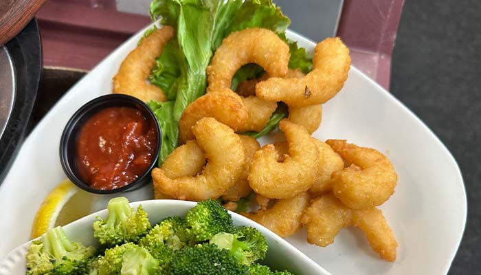 A plate of golden-fried shrimp on a bed of lettuce, served with a lemon wedge, broccoli, and cocktail sauce—a delicious favorite at Sherwood Restaurant.